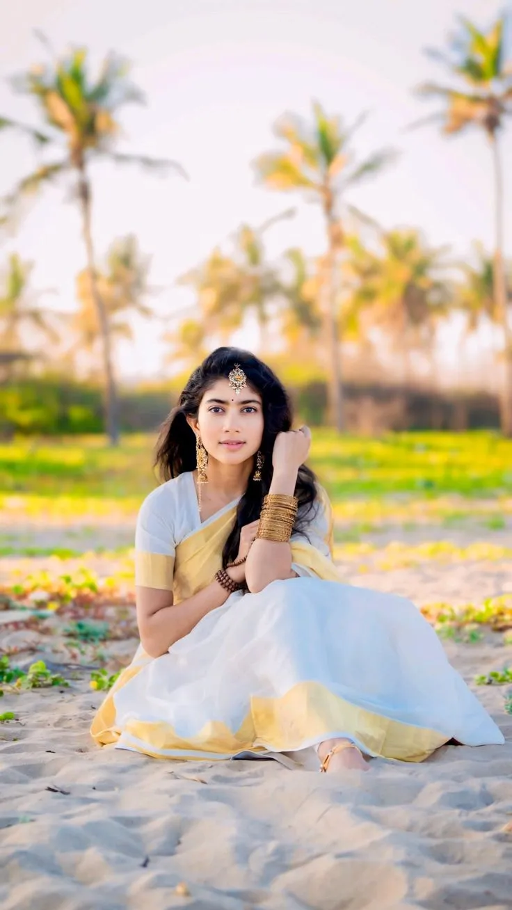 Sai Pallavi sitting on the beach sand wearing a kasavu saree