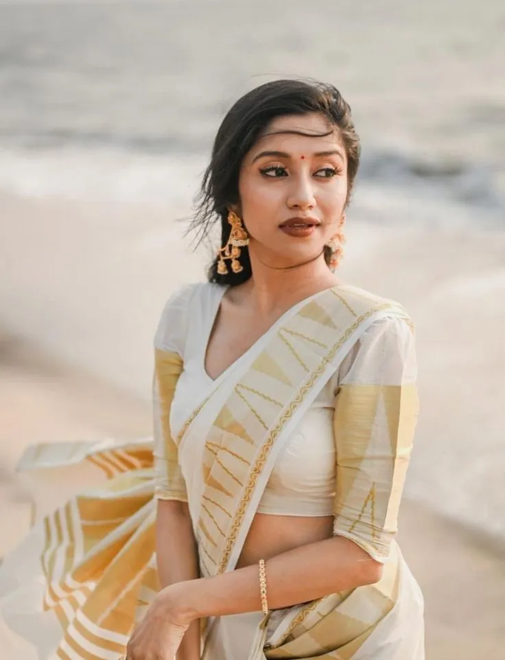 Shwetha Poornima in an Onam saree standing near the seawater