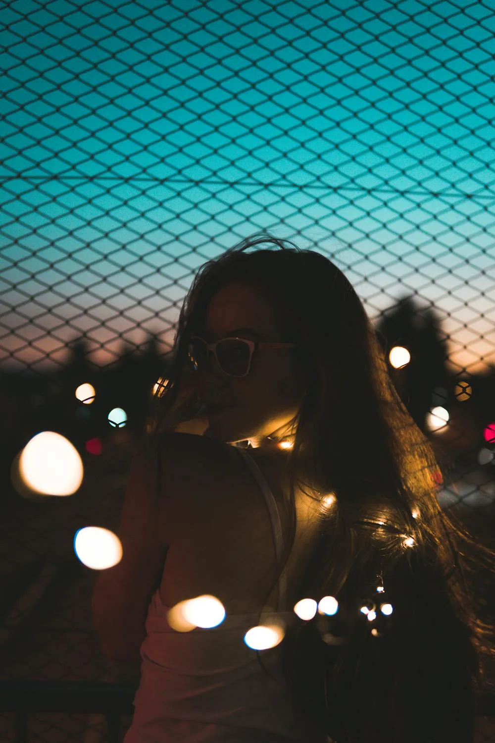 Silhouette of Woman with Fairy Lights At Dusk Behind a Fence