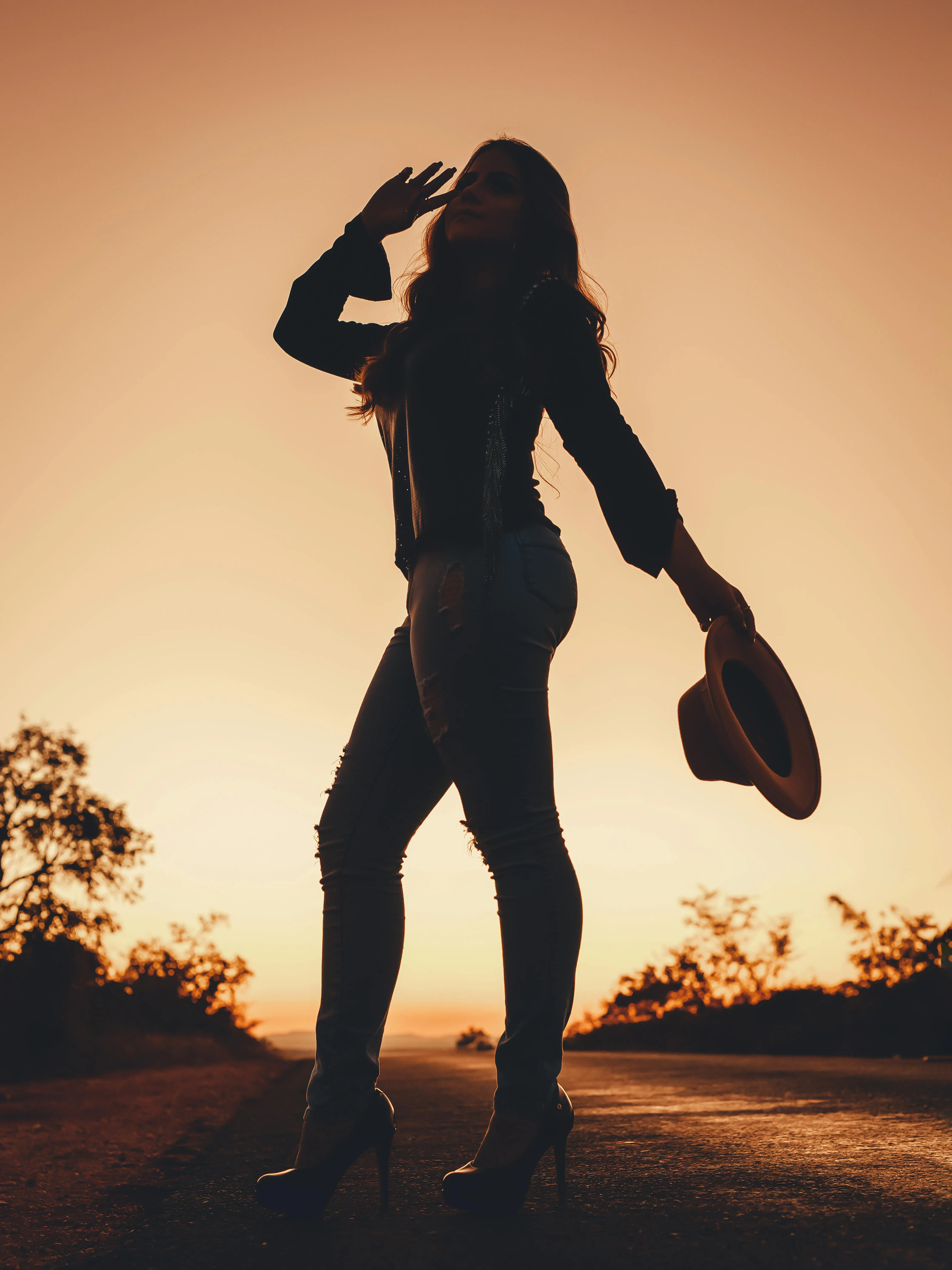 Silhouette of a Woman Holding a Hat At Sunset on the Road