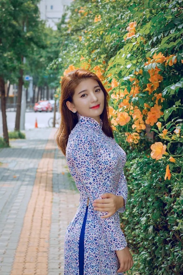 Smiling Woman in Floral Dress Posing Beside Vibrant Flowers
