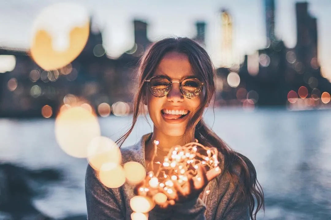 Smiling Woman Holding a Sparkler by the Waterfront At Night