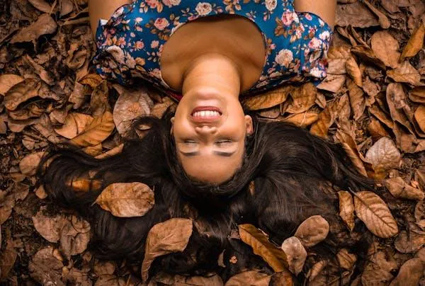 Smiling Woman Lying on an Autumn Leaf in a Floral Dress
