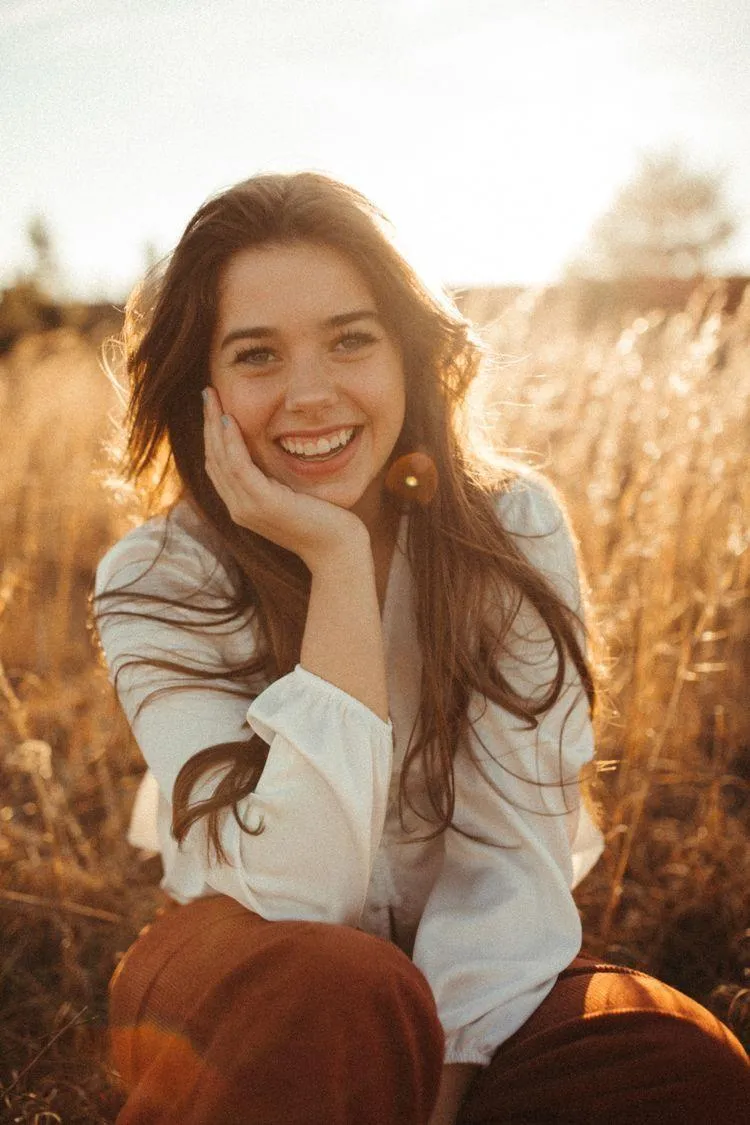 Smiling Woman Sitting in a Golden Field During Sunny Day