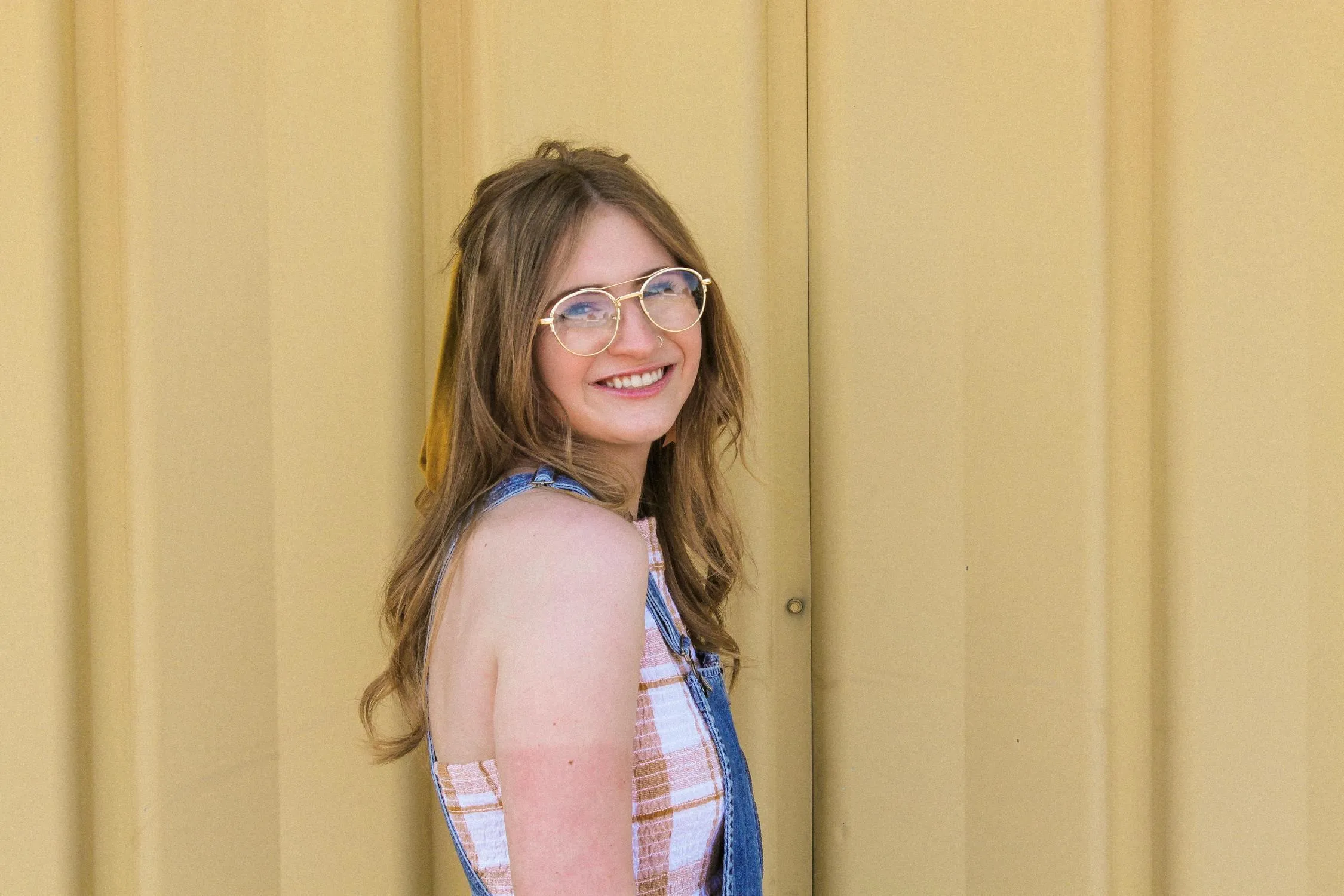Smiling Young Woman in Glasses Near a Yellow Wall Wallpaper