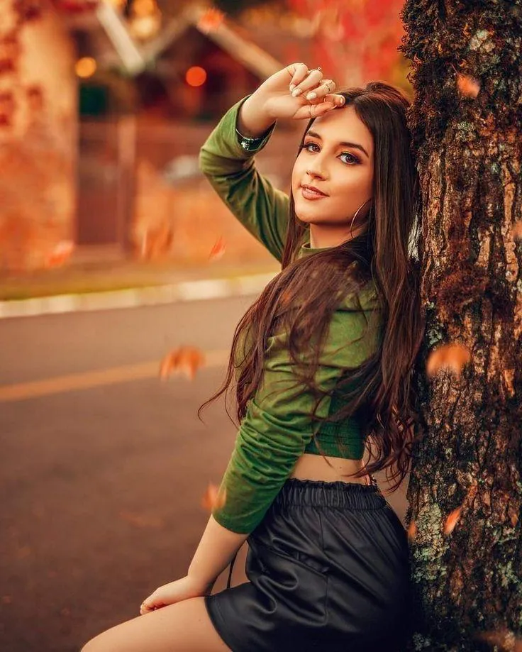Stylish Girl Leaning on a Tree in a Green Top in the Evening