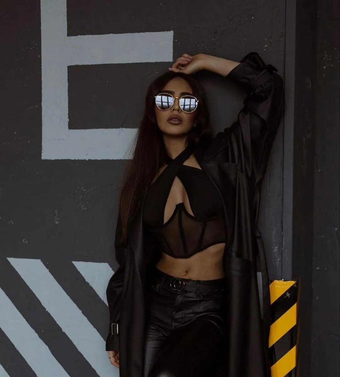 Stylish Woman in a Black Dress Against an Industrial Wall