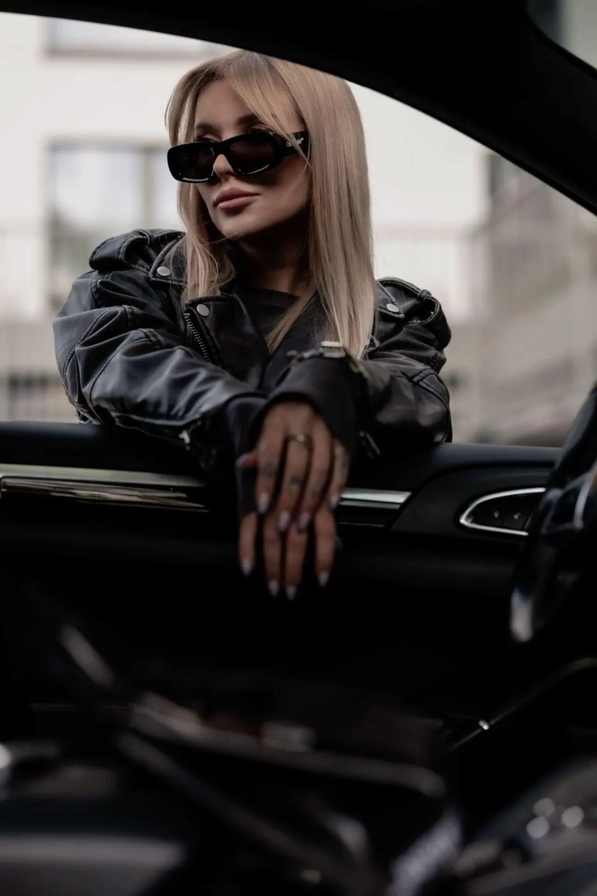 Stylish Woman in Sunglasses and Leather Jacket by Car Window