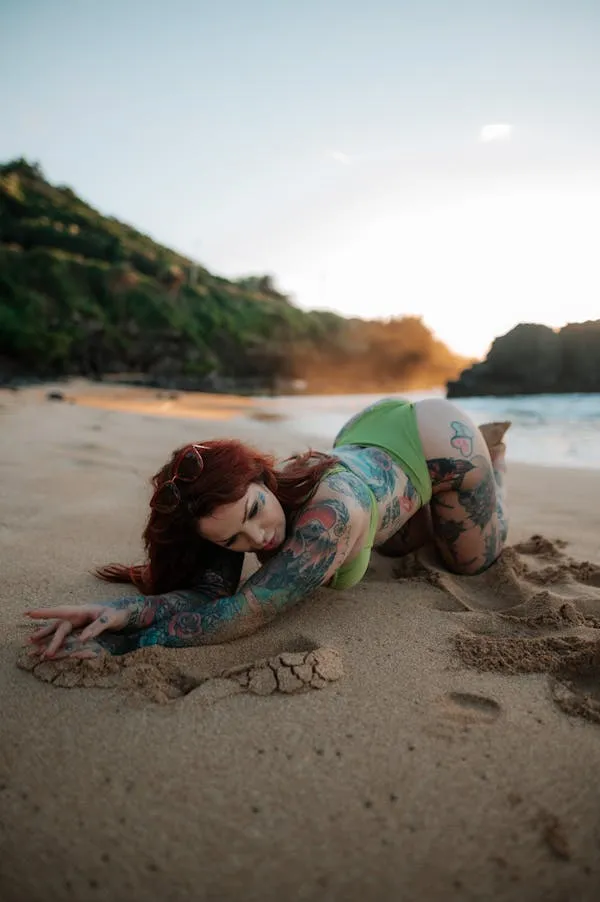 Tattooed Woman Lying on a Sandy Beach During Golden Light
