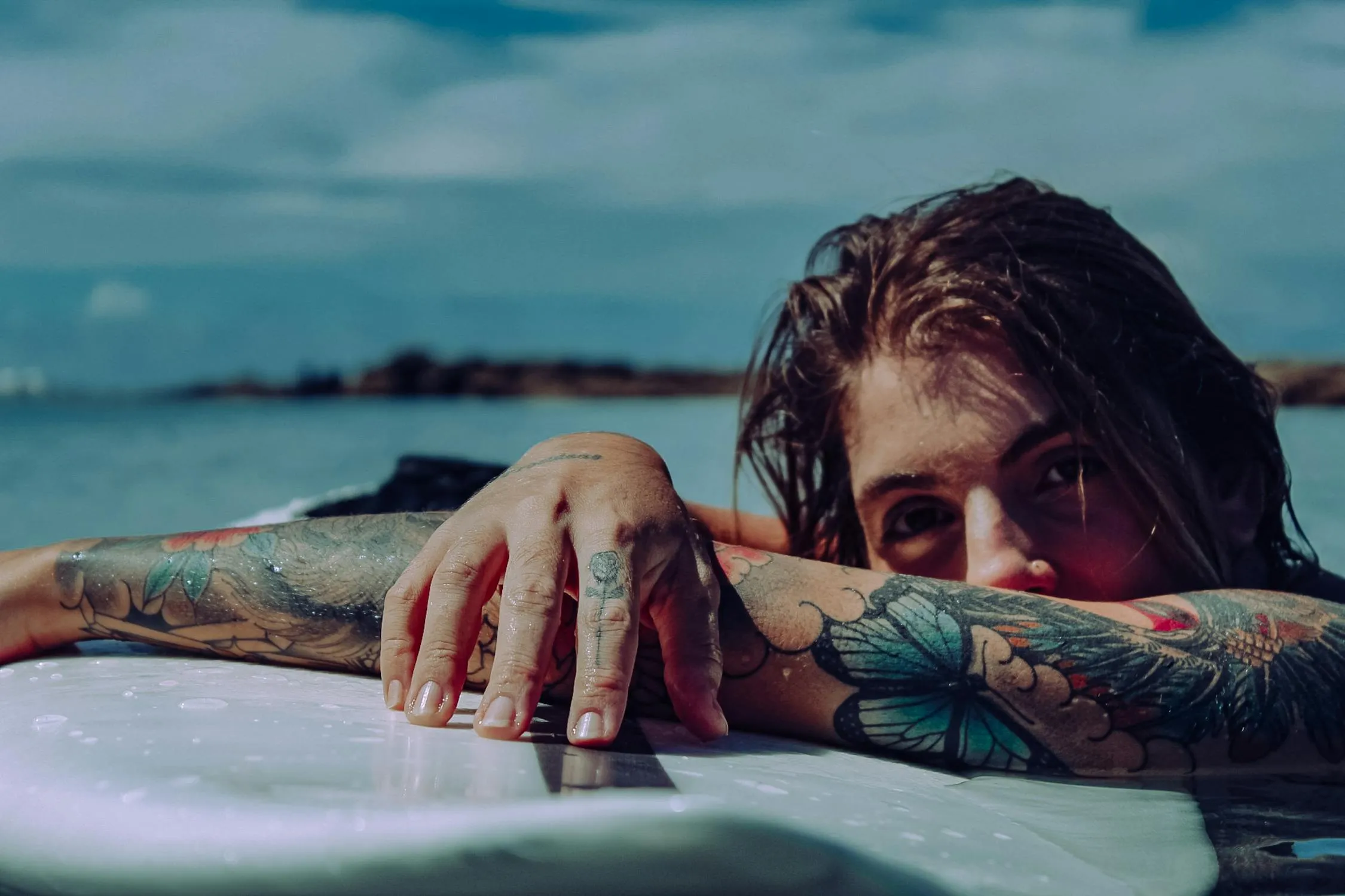 Tattooed Woman Resting Arms on Pool Edge with Ocean Backdrop