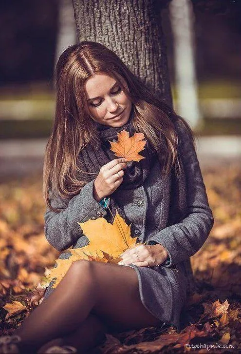 Thoughtful Model Sitting in Autumn Park with Fallen Leaves