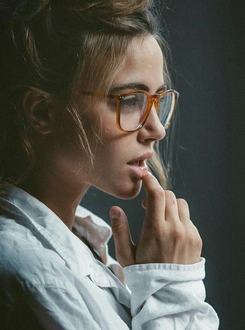 Thoughtful Young Woman with Glasses Sitting Near the Window