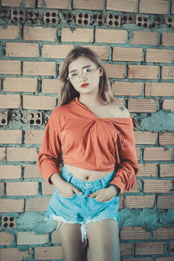 Trendy Woman in Orange Top and Denim Posing by a Brick Wall