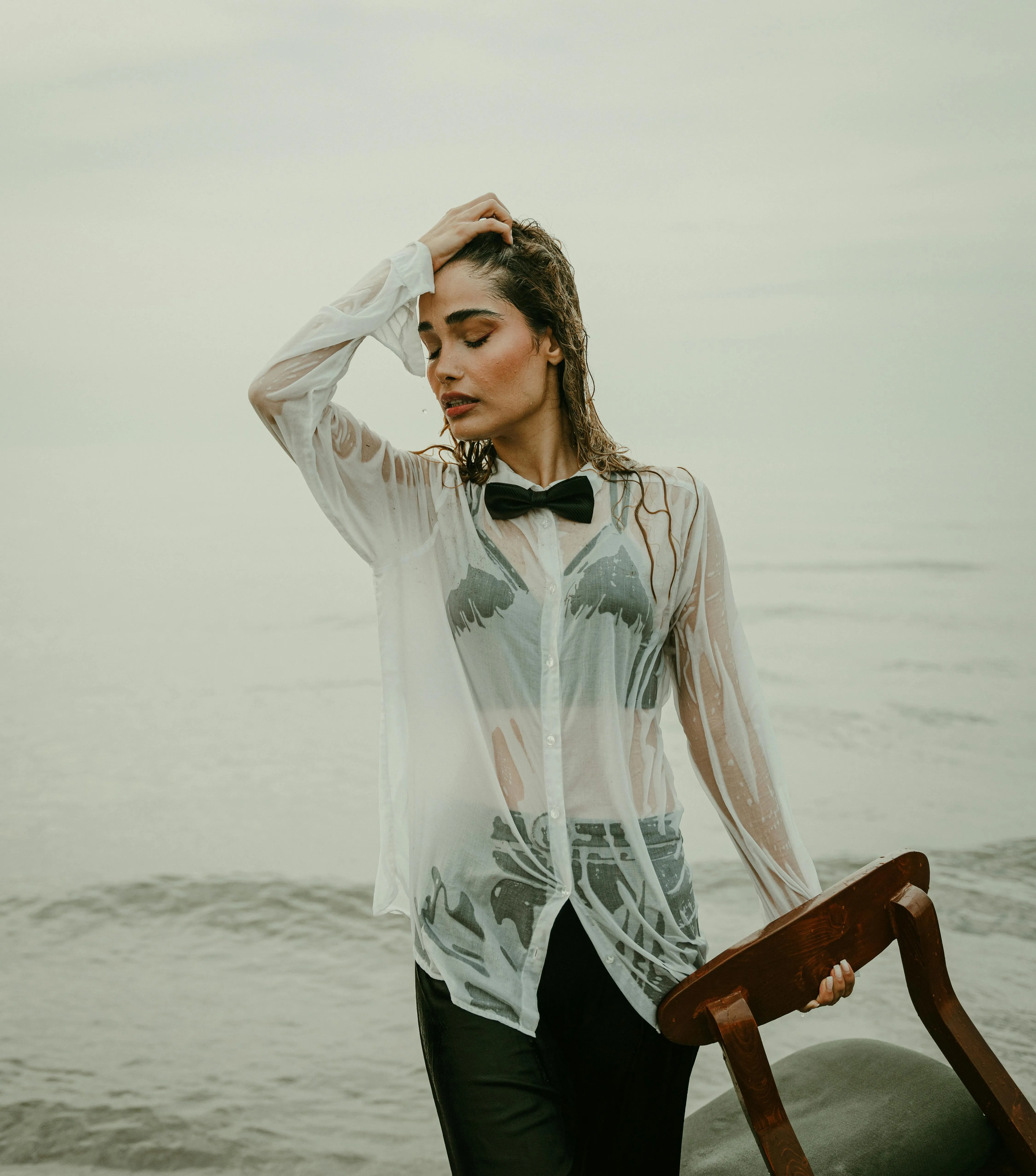 Wet Look Fashion Model in a Shirt Posing with a Chair At Sea