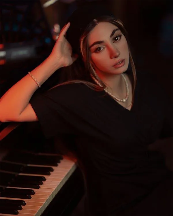 Woman in a Black Dress Posing by a Piano in Dim Lighting