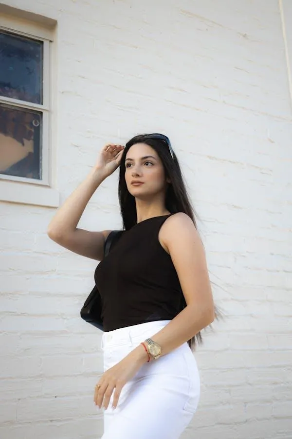 Woman in a Black Top Posing Confidently by a White Wall