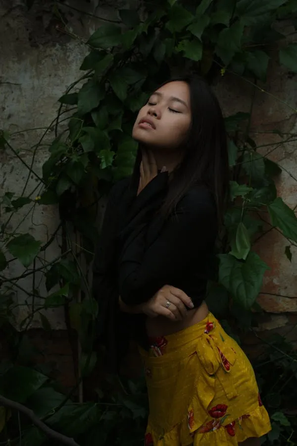 Woman in a Black Top and Yellow Skirt Near a Leafy Wall