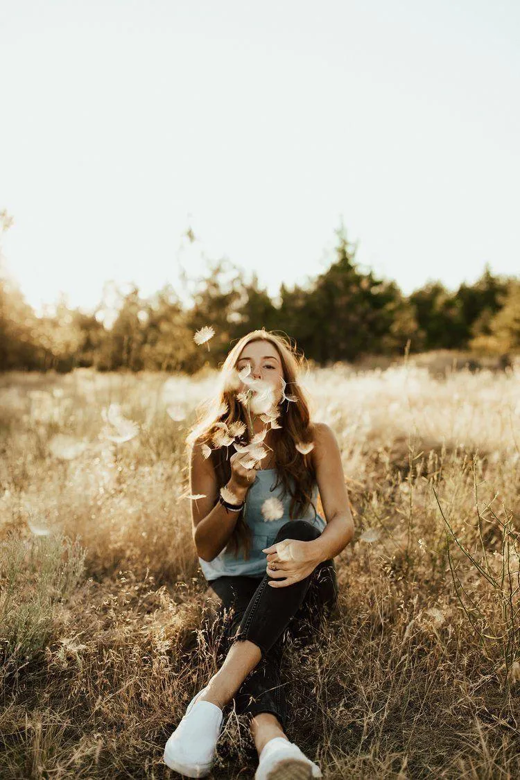 Woman Blowing Dandelion Seeds in a Golden Grassy Field Image