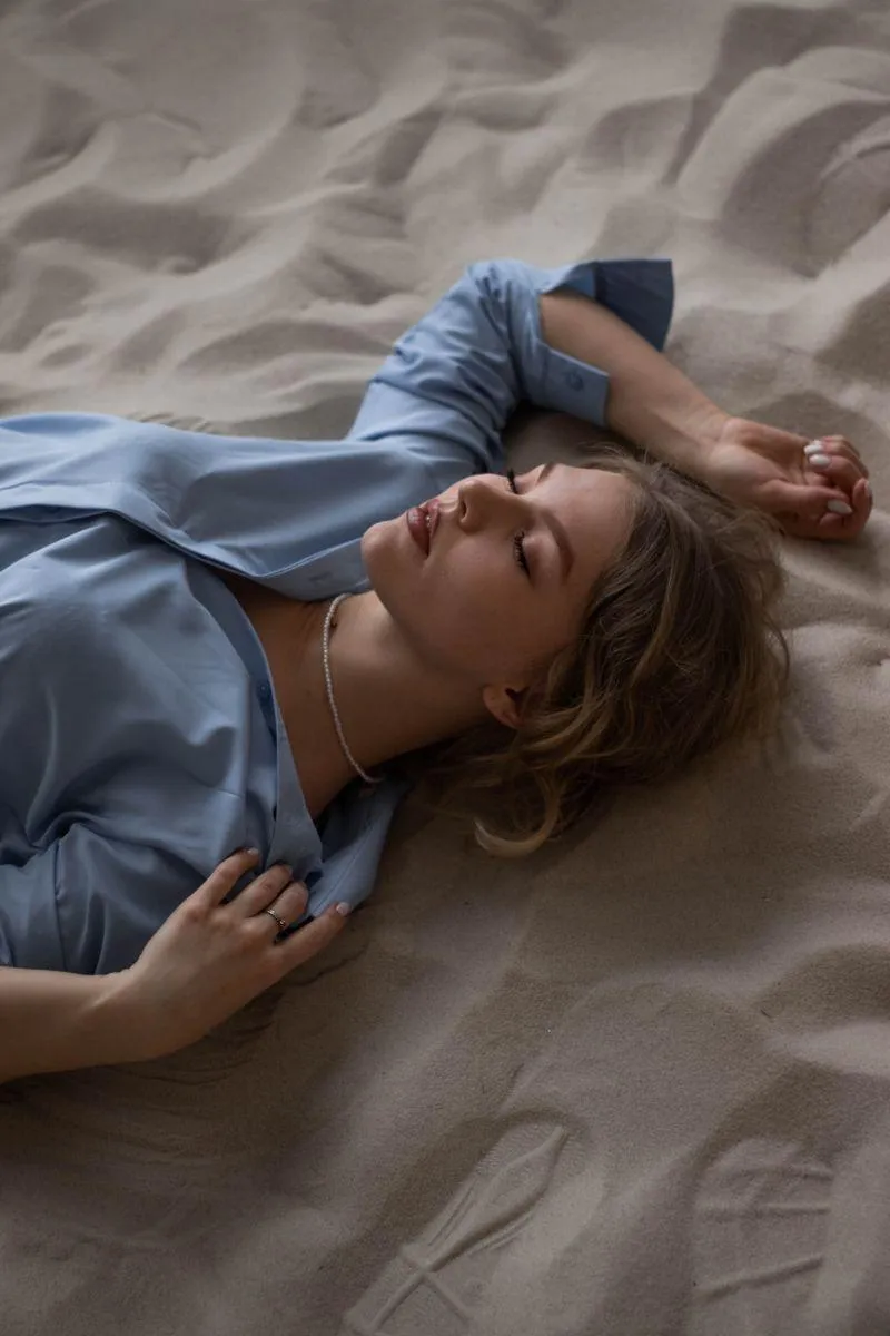 Woman in a Blue Shirt Lying on Bed with Hand Near Her Head