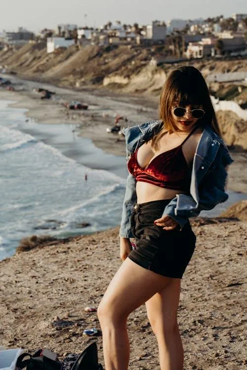 Woman in a Denim Jacket and Shorts Posing by the Ocean Shore