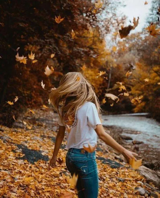 Woman Exploring a Rocky Beach Covered in Yellow Fall Leaves
