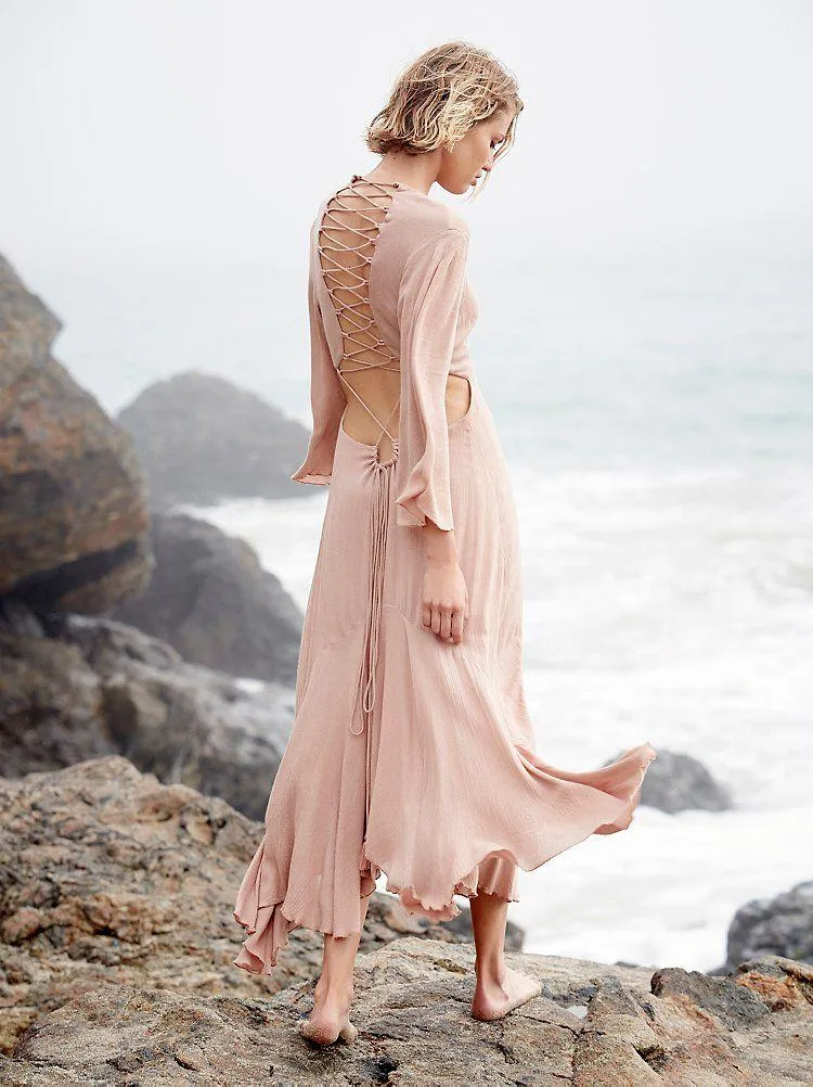 Woman in a Flowing Dress Standing Near a Rocky Ocean Shore