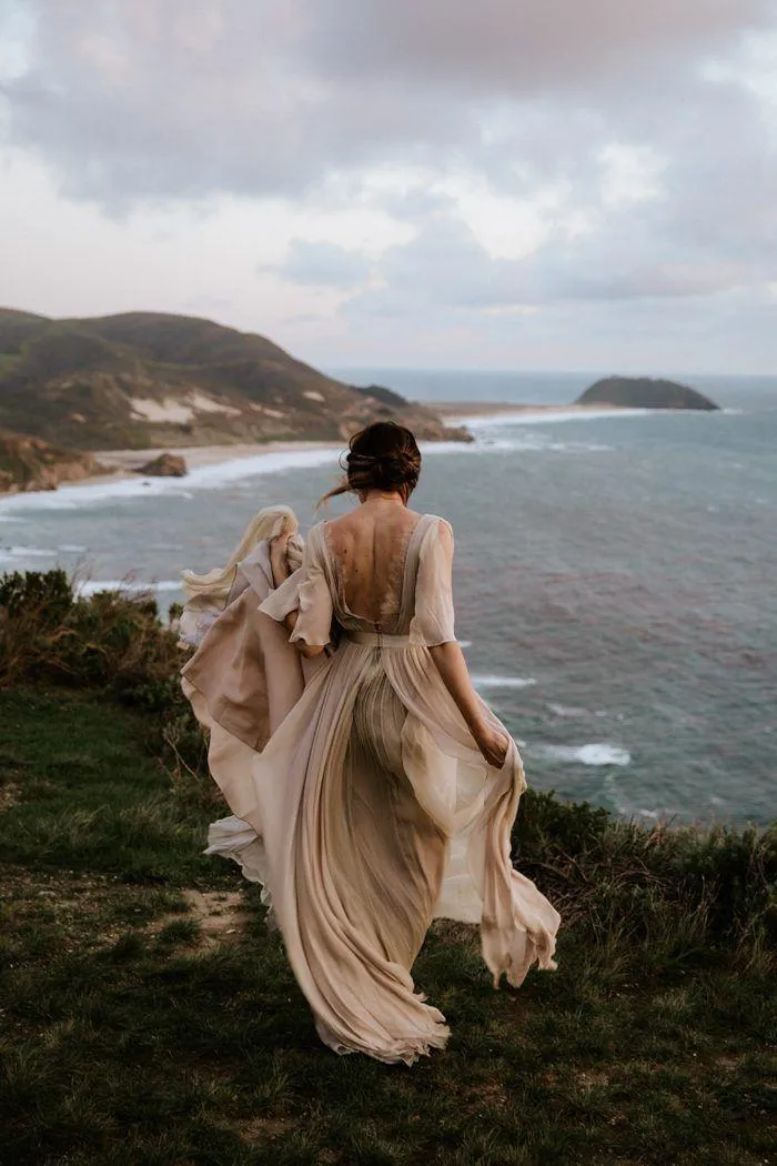 Woman in a Flowing Dress Standing Near the Ocean Cliffs