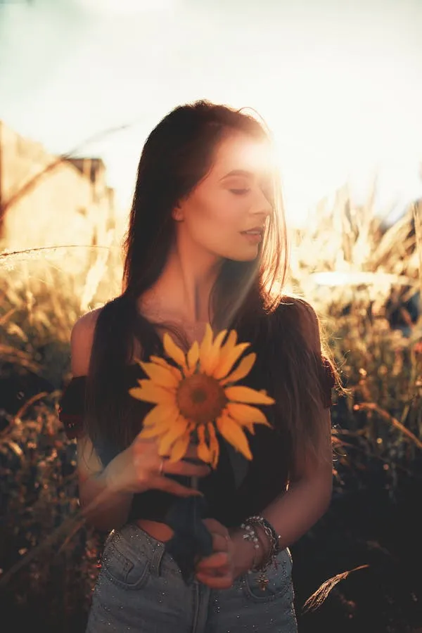 Woman Holding a Sunflower in the Sunlit During Golden Hour