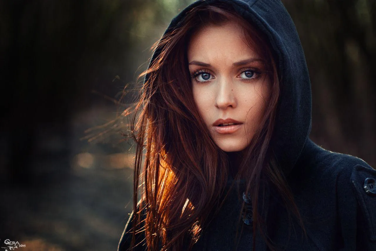 Woman in Hoodie with Piercing Gaze in a Dark Outdoor Setting