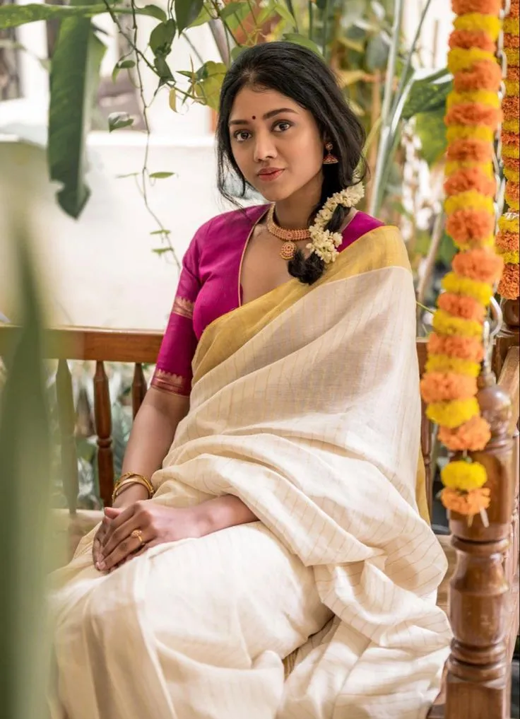 Woman in a checked white saree and pink blouse near a flower
