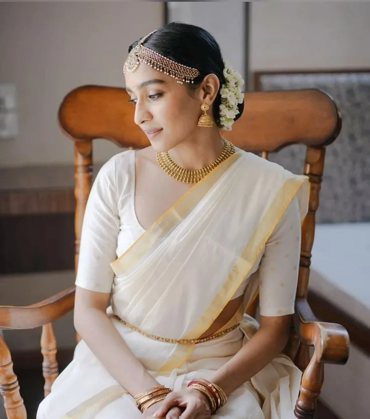 Woman in a kasavu saree sitting on a chair looking down