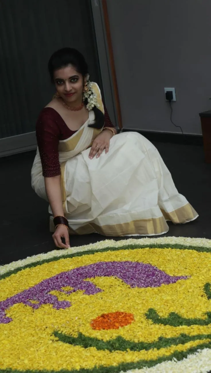 woman in a Kerala Kasavu saree decorating the flower kolam