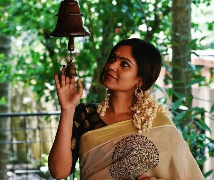 Woman in a Kerala saree with her hand on the temple bell