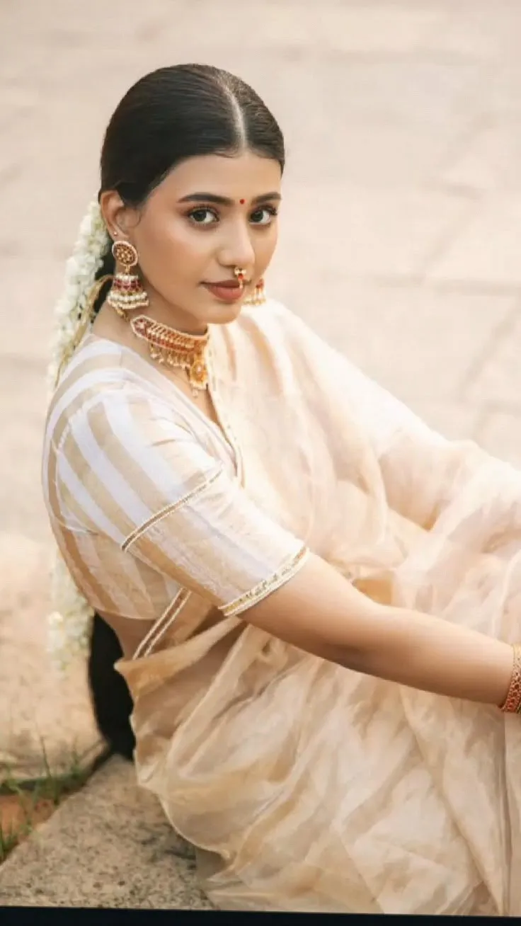Woman in a white and gold striped saree sitting outdoors