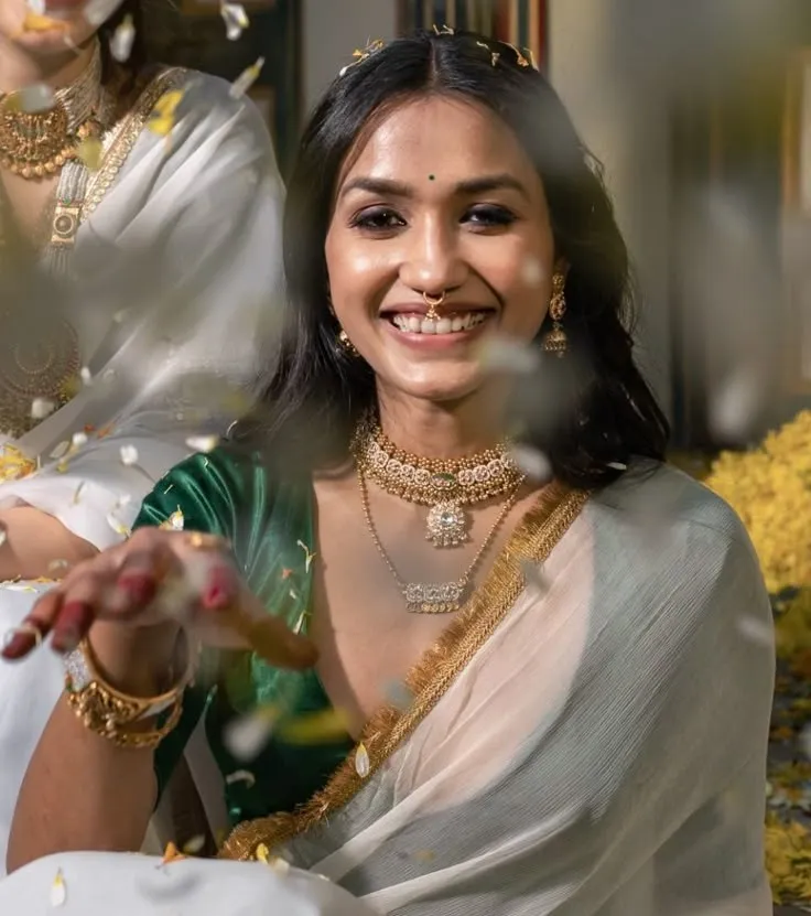 woman in a white Kerala saree sitting with a cute smile
