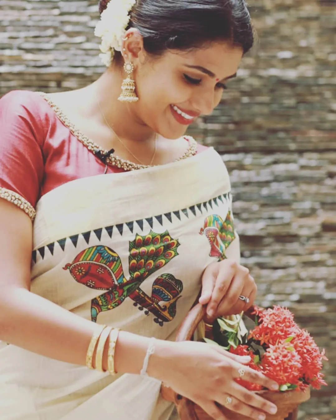 Woman in a white saree holding a basket with red flowers