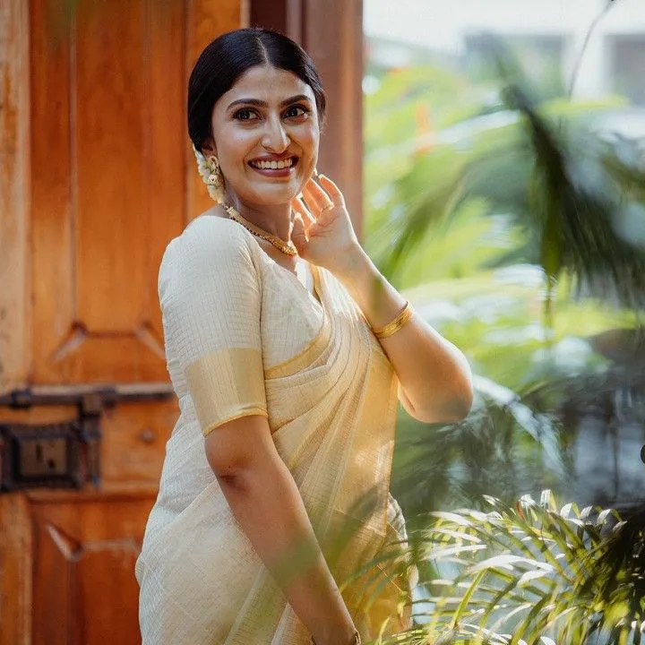 Woman in a white saree standing near the brown doors image