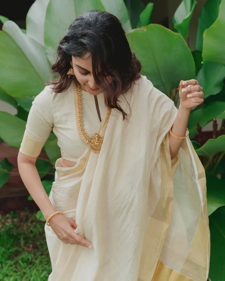 woman in a white saree standing near the green leaves image