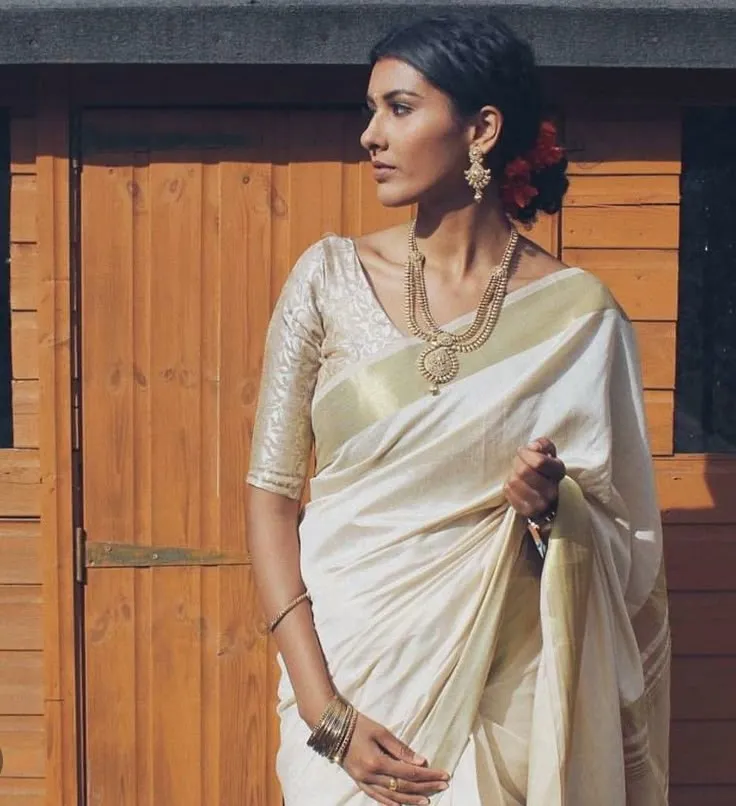 Woman in a white saree standing near the orange background