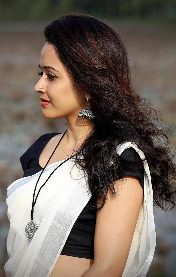 Woman in a white saree with a black blouse looking sideways