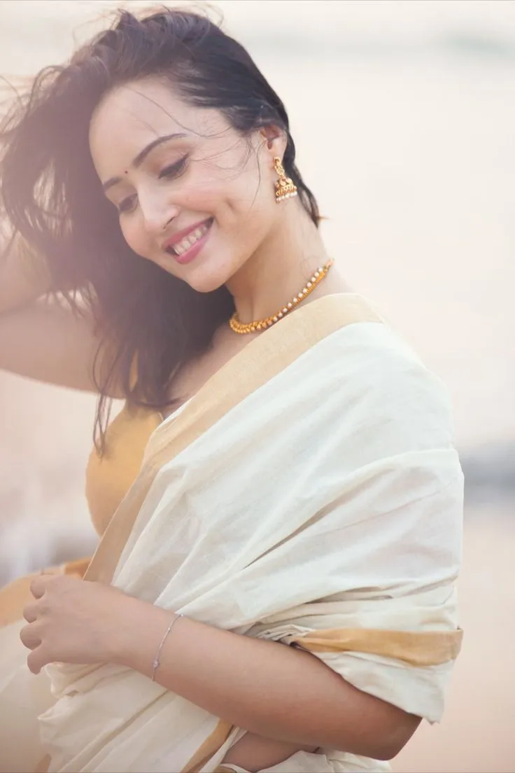 Woman in a white saree with a golden jacket and a smile