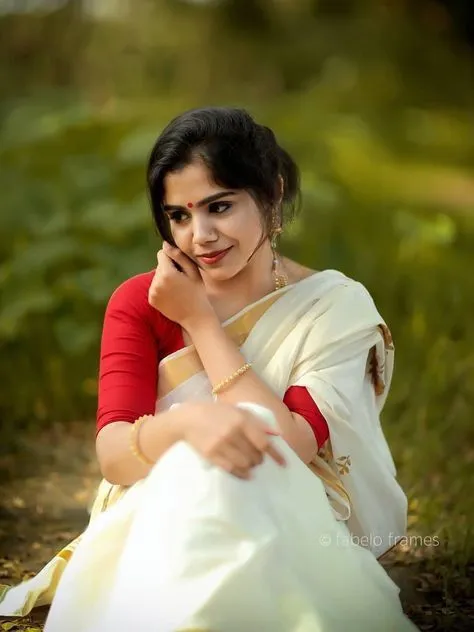 Woman in an Onam saree and red jacket her hand on her cheek