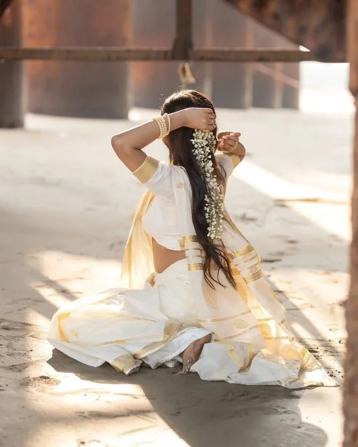 Woman in an Onam saree sitting on the floor with flowers