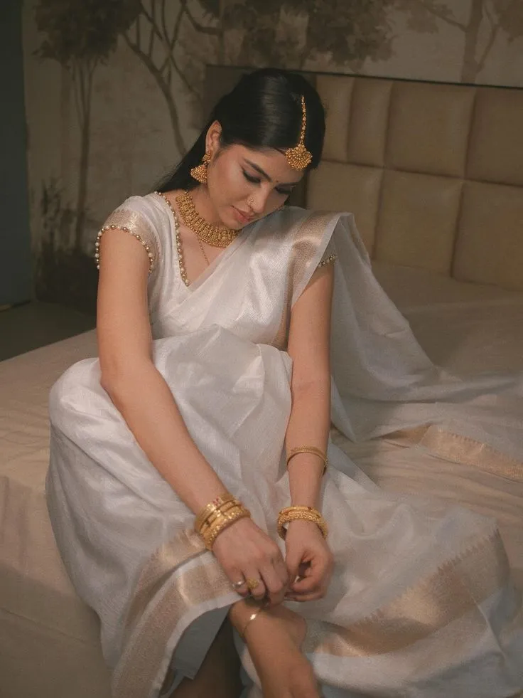 Woman in white saree sitting on the bed with hand on her leg
