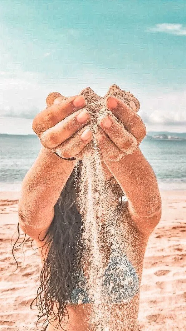 Woman Letting Sand Fall Through Her Hands on a Sunny Beach