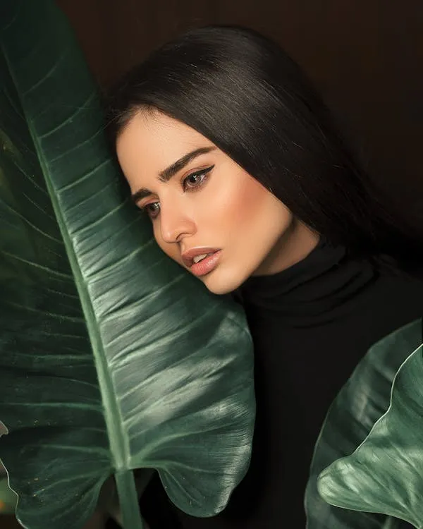 Woman with Long Hair Posing Next To Large Green Leaf Indoors