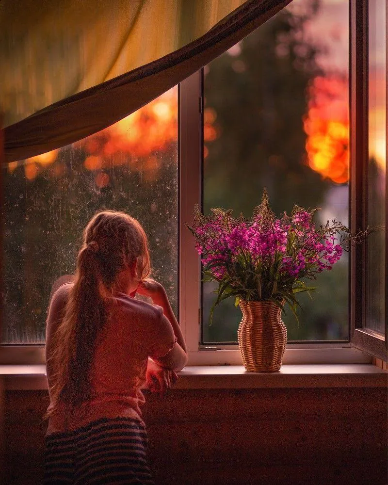 Woman Looking Out the Window with Flowers and Warm Lighting