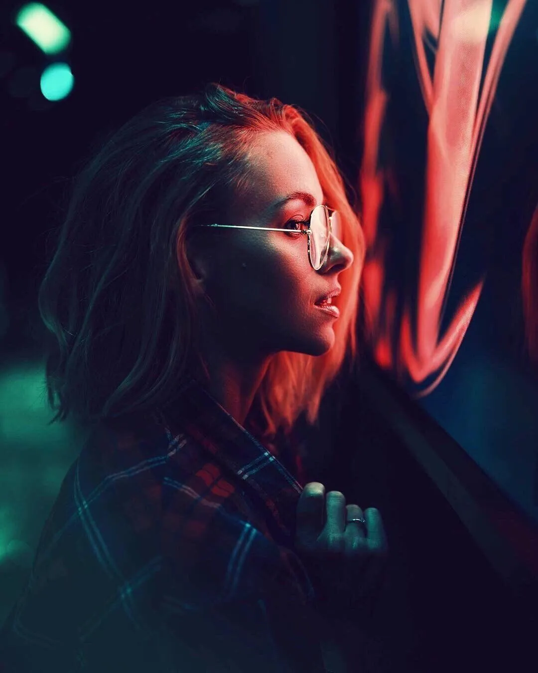 Woman Looking Through a Glass Lit by Red and Teal Lights
