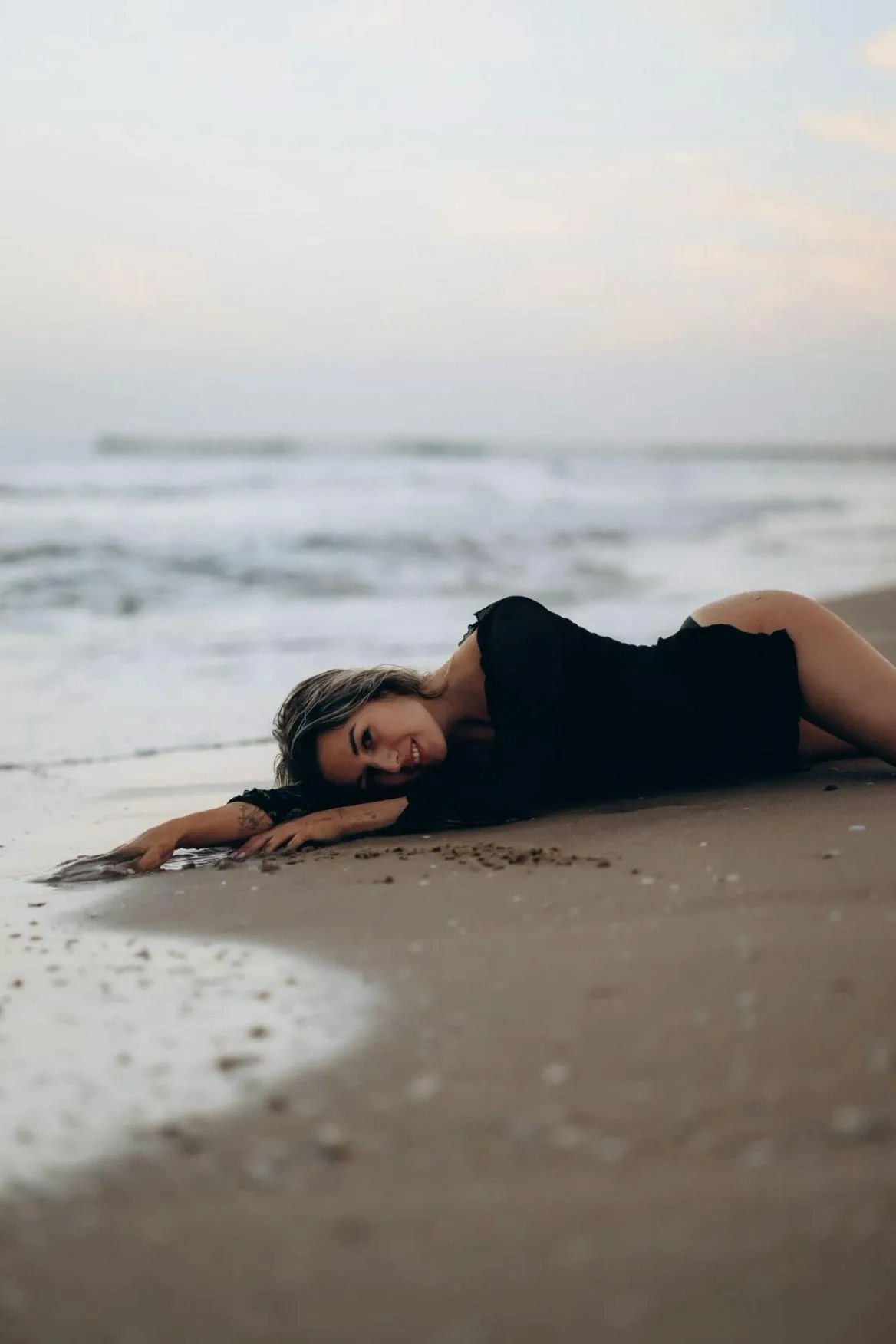Woman Lying on a Sandy Beach in a Black Dress Free Wallpaper