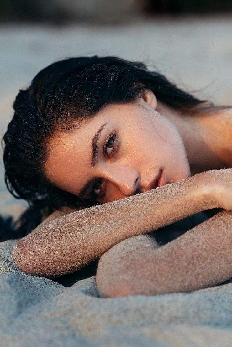 Woman Lying on the Sand with Wet Hair Looking Into Camera